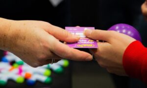Close up of a hand passing a purple Meic business card over to another hand