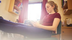 Girl in university bedroom sat with feet up and book in hand