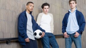 Three boys leaning against a wall holding a football
