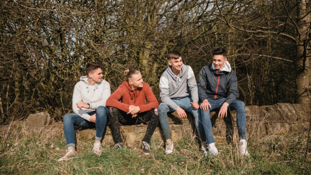 Teen boys smiling and talking whilst sat around outside on a low brick wall
