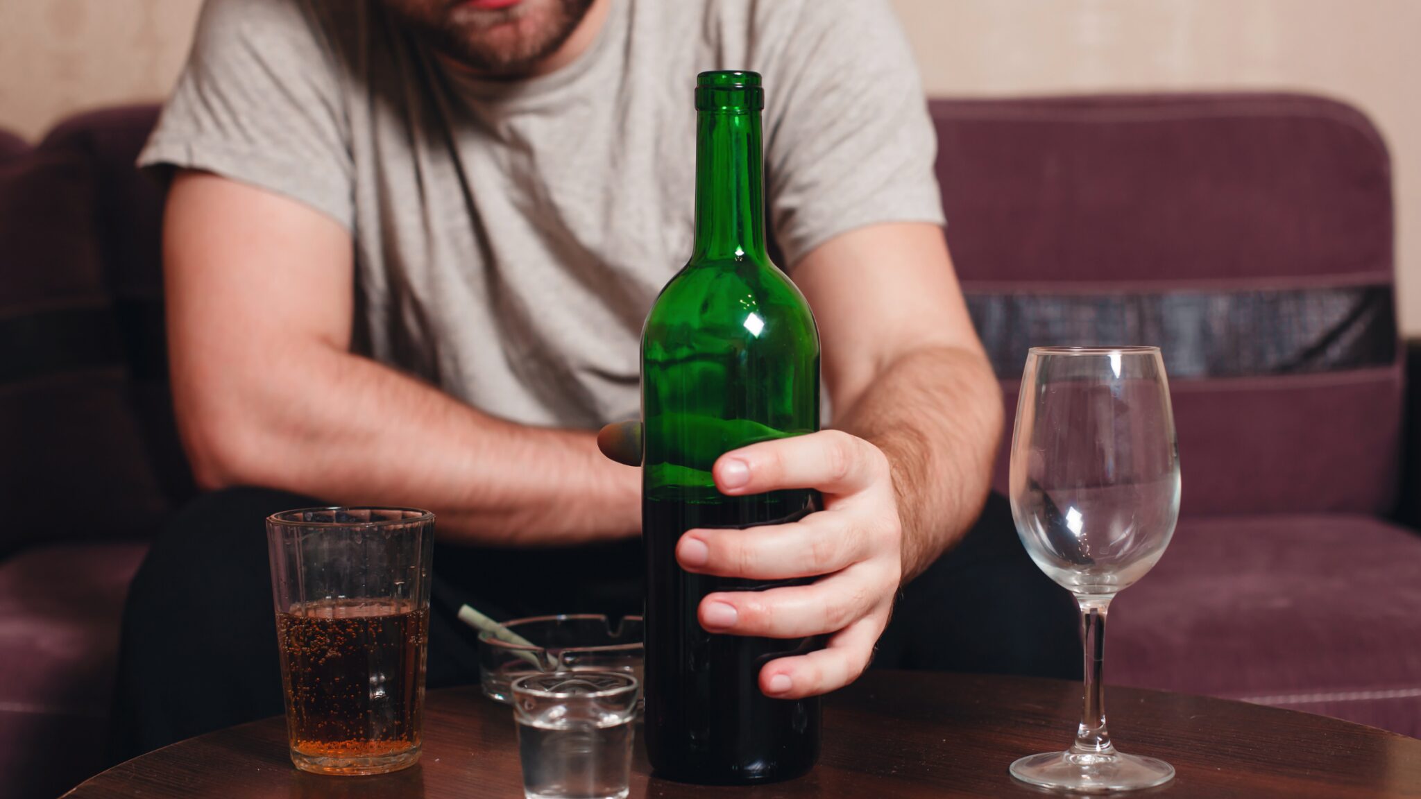 A man sitting on a sofa and holding a half empty bottle of wine