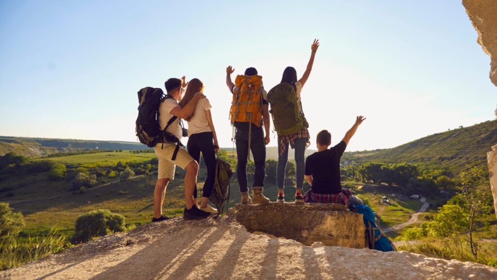 Group of 5 teenagers stand at the edge of a cliff on a sunny day with blue skies. They have their fists in the air, in celebration. 