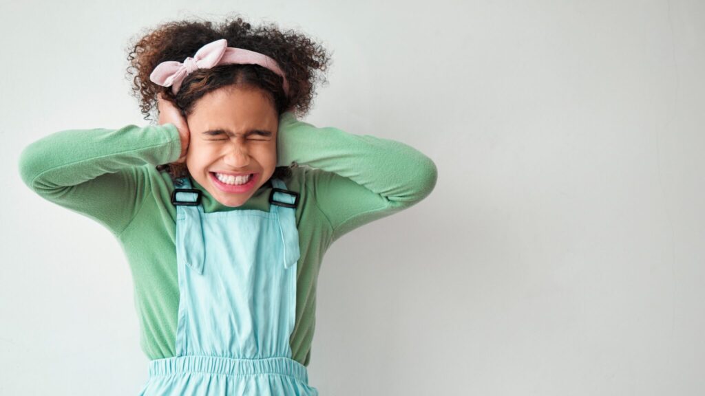 Young girl covering her ears in pain as there's too much noise
