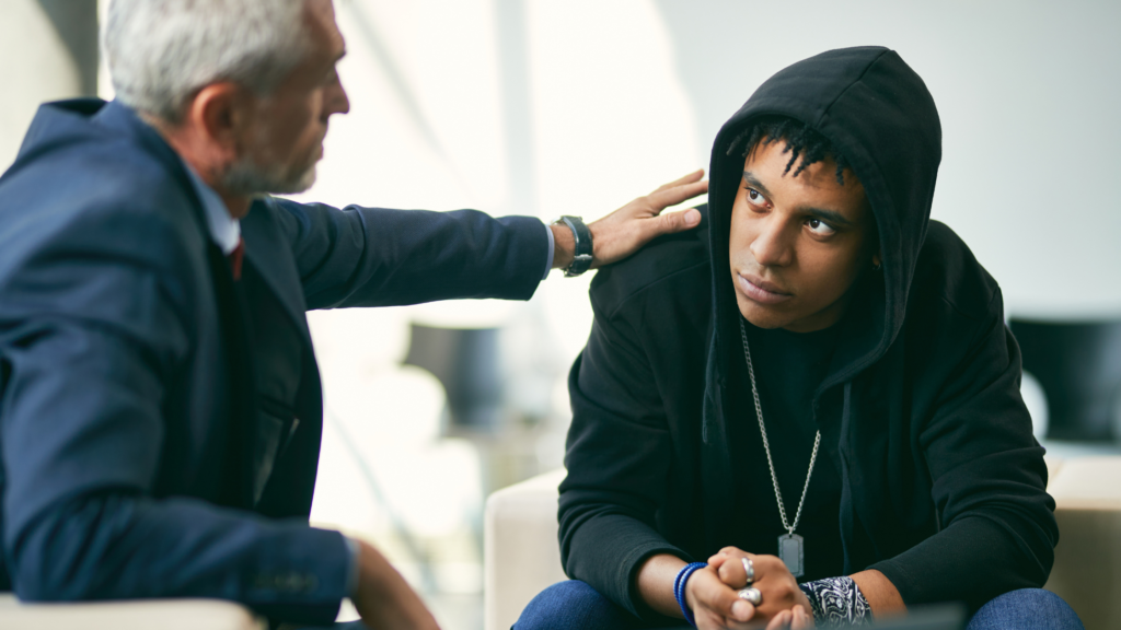 Teen boy looks sadly at a therapist whilst he is being consoled with a hand on his shoulder