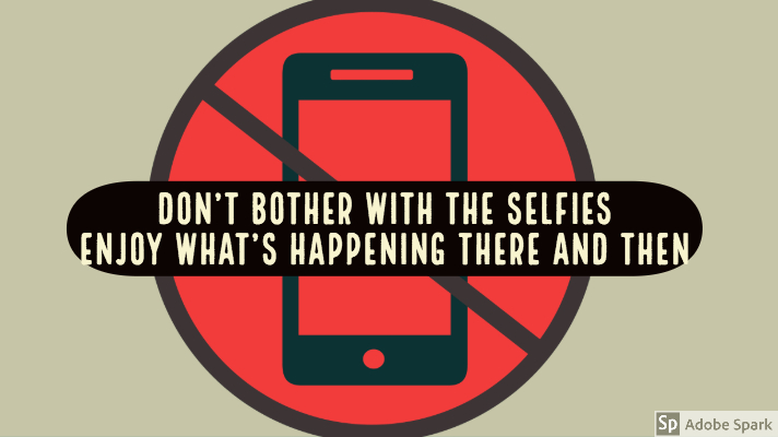 A warning sign, red circle with image of a mobile phone crossed out. The words "Don't bother with the selfies; enjoy what's happening there and then" are on the image.