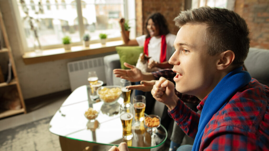 Excited people watching sport match at home. The table is filled with alcohol drinks, suggesting they've been binge drinking