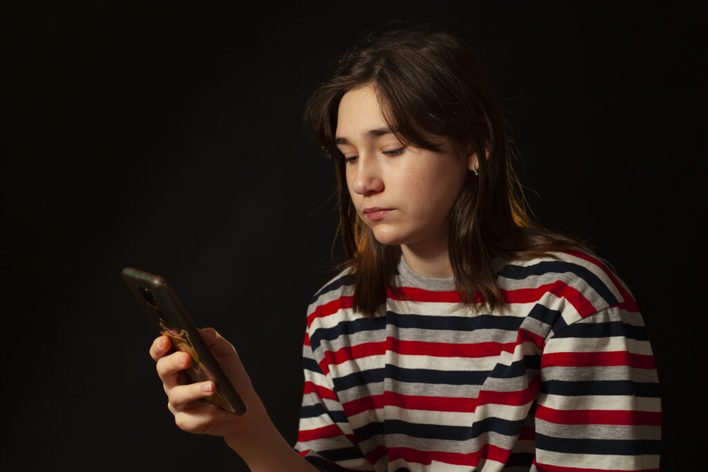 Teenage girl looks at her phone, she looks sad.