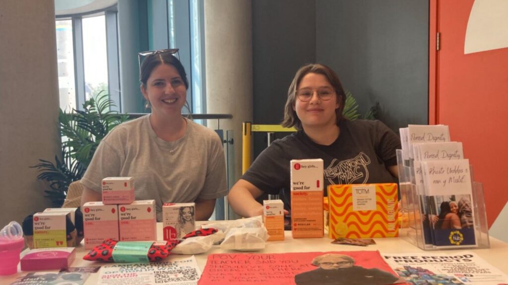 Two people sat behind a stall full of reusable period products