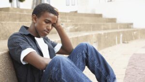 Teen boy sat slouched against some steps looking sad