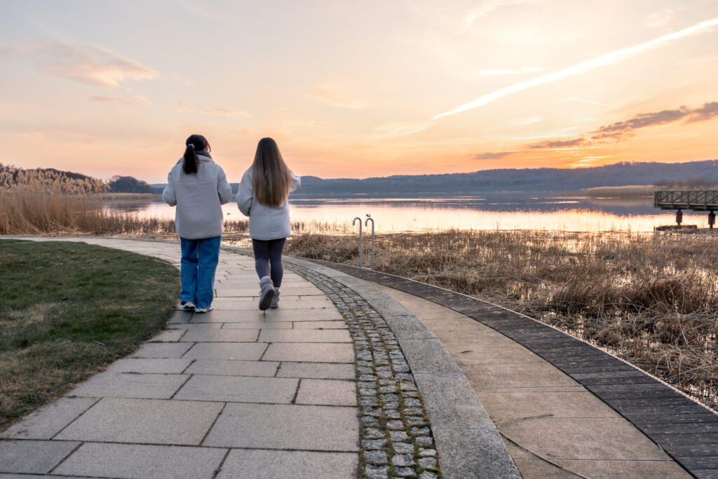 Two women walking together along a promenade at sunset