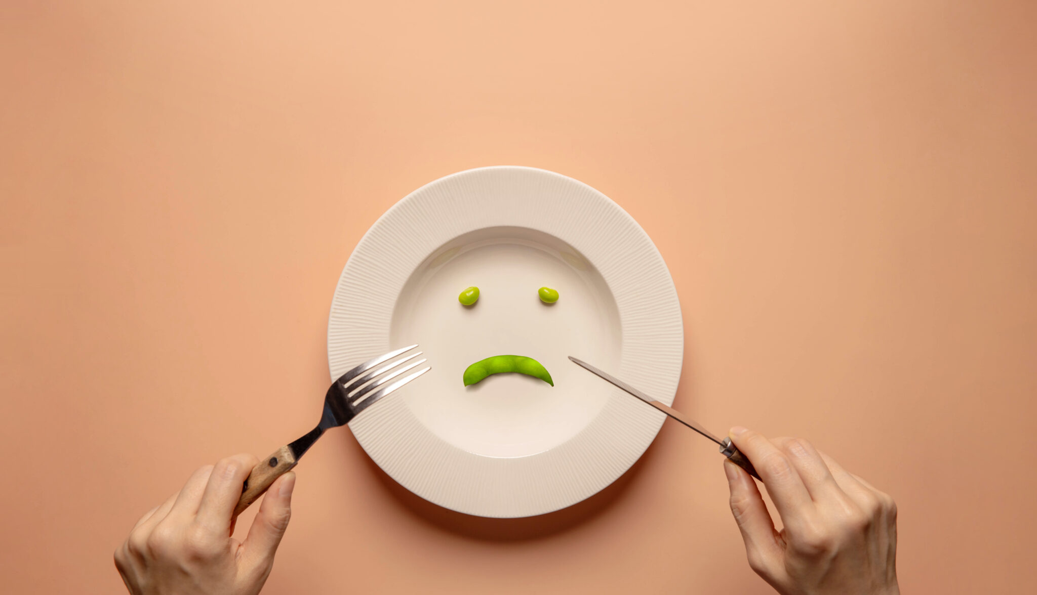 Young Woman Using Fork and Knife to Eating Green Soy Bean on Plate.